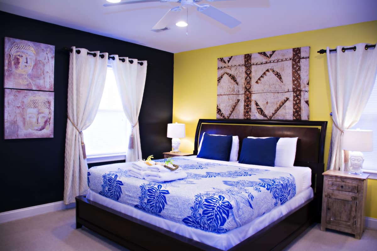 A neatly made bed with a floral bedspread, a bedside table with a lamp, and artwork on the walls.