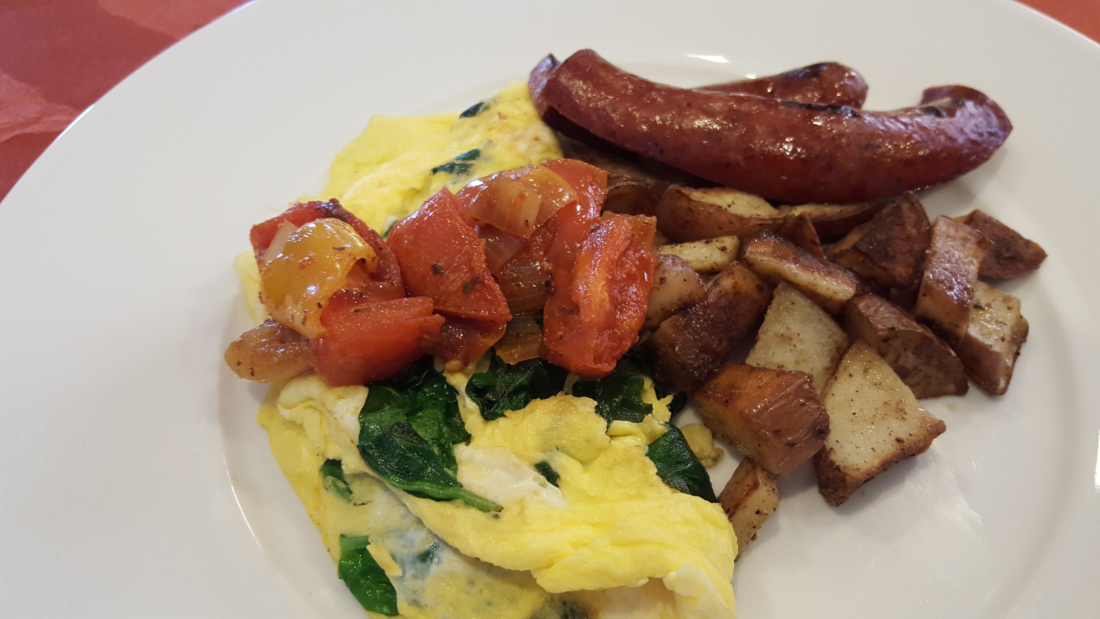 A plate with scrambled eggs, sautéed tomatoes, sausage, and roasted potatoes.