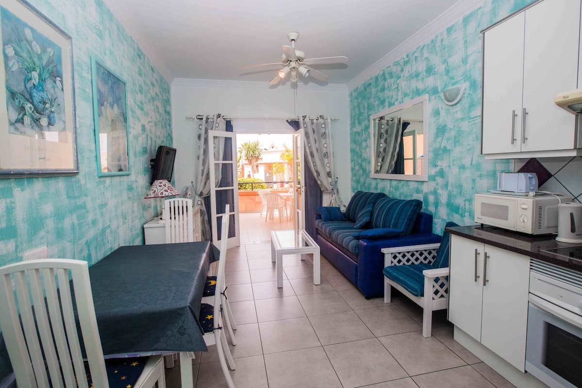 A compact living space with a dining area, a sofa, a kitchenette, and a ceiling fan.