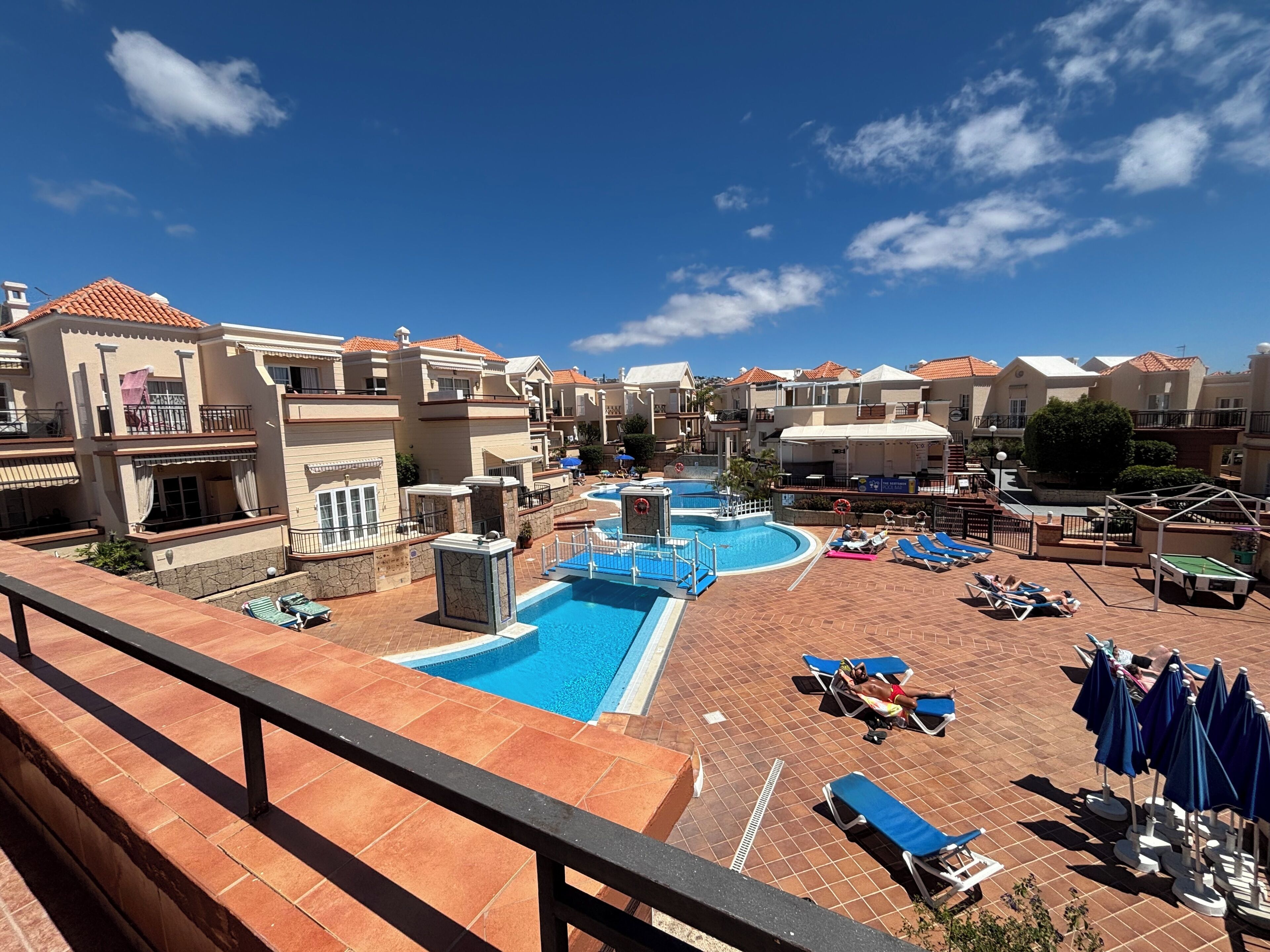 A resort with a swimming pool, sun loungers, and a view of the surrounding buildings.