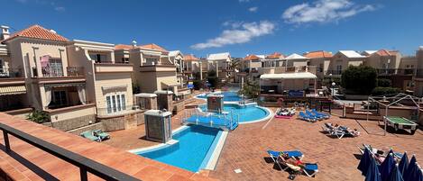 A resort with a swimming pool, sun loungers, and a view of the surrounding buildings.