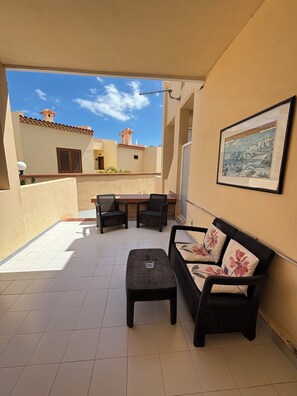 Un patio cubierto con una mesa y sillas, un sofá de mimbre y un cuadro en la pared.