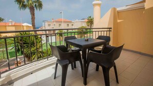 A balcony with a table and chairs, a palm tree, and a view of buildings and a tower. - Yucca Park Aparthotel (Adeje)