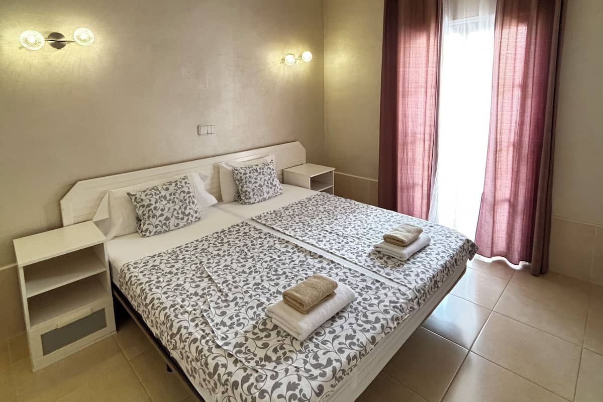 A bedroom with a bed, bedside tables, a ceiling fan, and curtains.