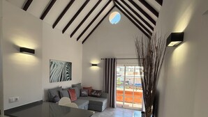 A modern living space with a dining area, a sofa set, a large window, and a decorative plant. - Yucca Park Aparthotel (Adeje)