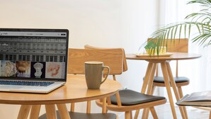 A laptop on a wooden table with a mug, a chair, and a plant in a bright room. - Residence Leopoldo (Florence)
