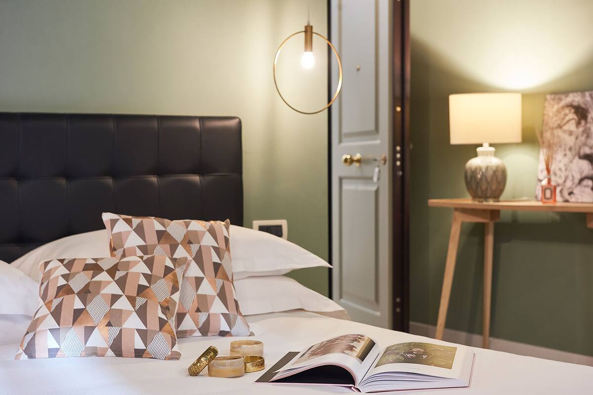 A neatly made bed with patterned pillows, a bedside table with a lamp, and a framed picture on the wall.