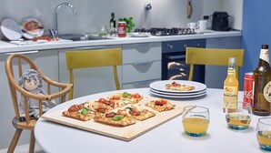 A modern kitchen with a pizza on a wooden board, a dining table with plates, and a few bottles and glasses. - Residence Leopoldo (Florence)