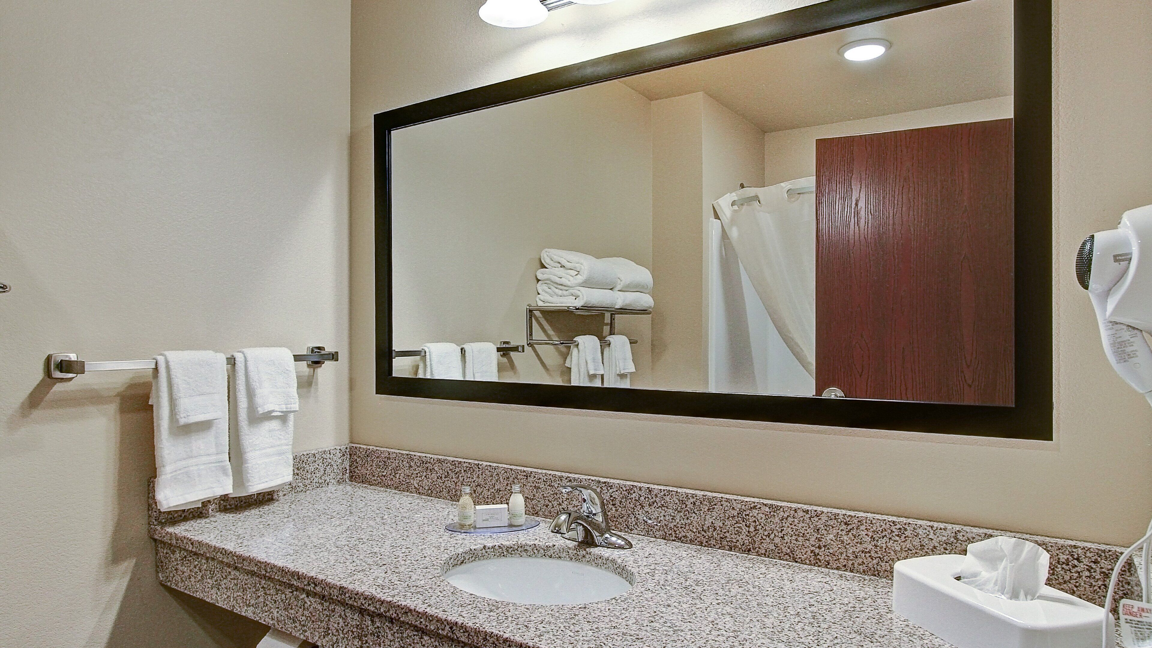 A bathroom with a sink, mirror, towel rack, and a shower area.