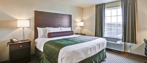 A hotel room with a large bed, two bedside lamps, a telephone, a nightstand, a window with curtains, and a radiator.
