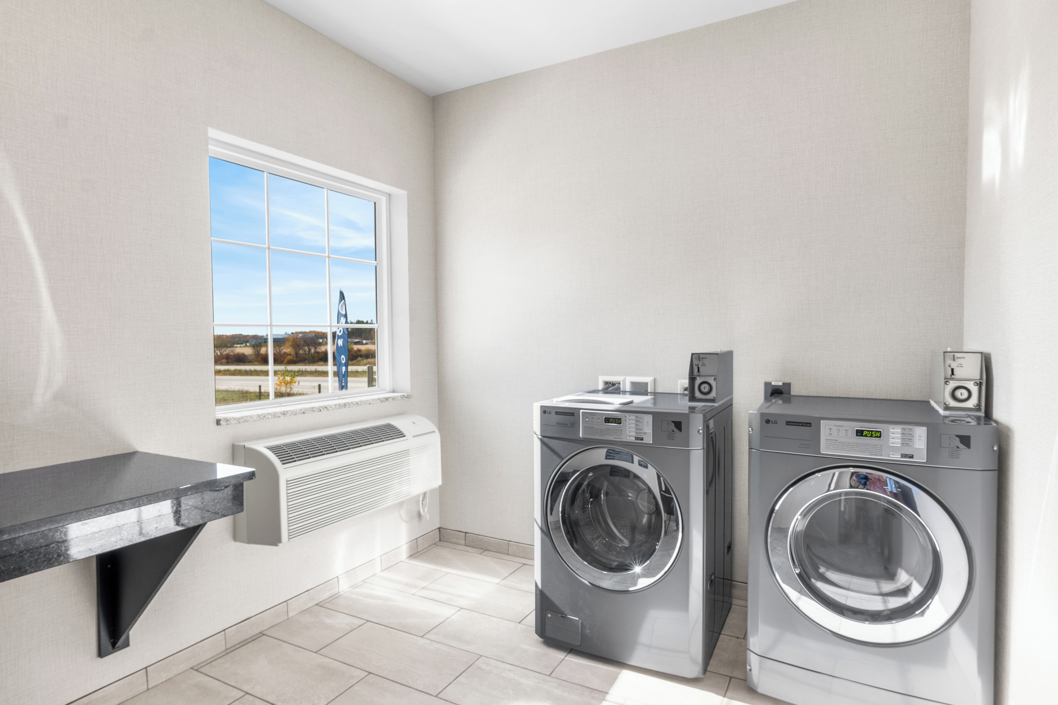 A laundry room with two washing machines, a window with a view, and a built-in air conditioning unit.