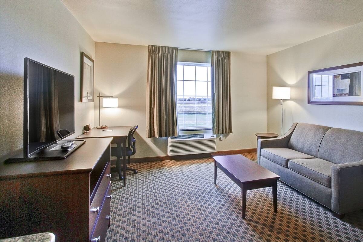 A hotel room with a bed, a desk with a chair, a sofa, a TV, and a window with curtains.