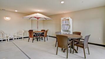 A dining area with a round table, chairs, and a white umbrella. There is a white bookshelf labeled "TOWELS" in the background.