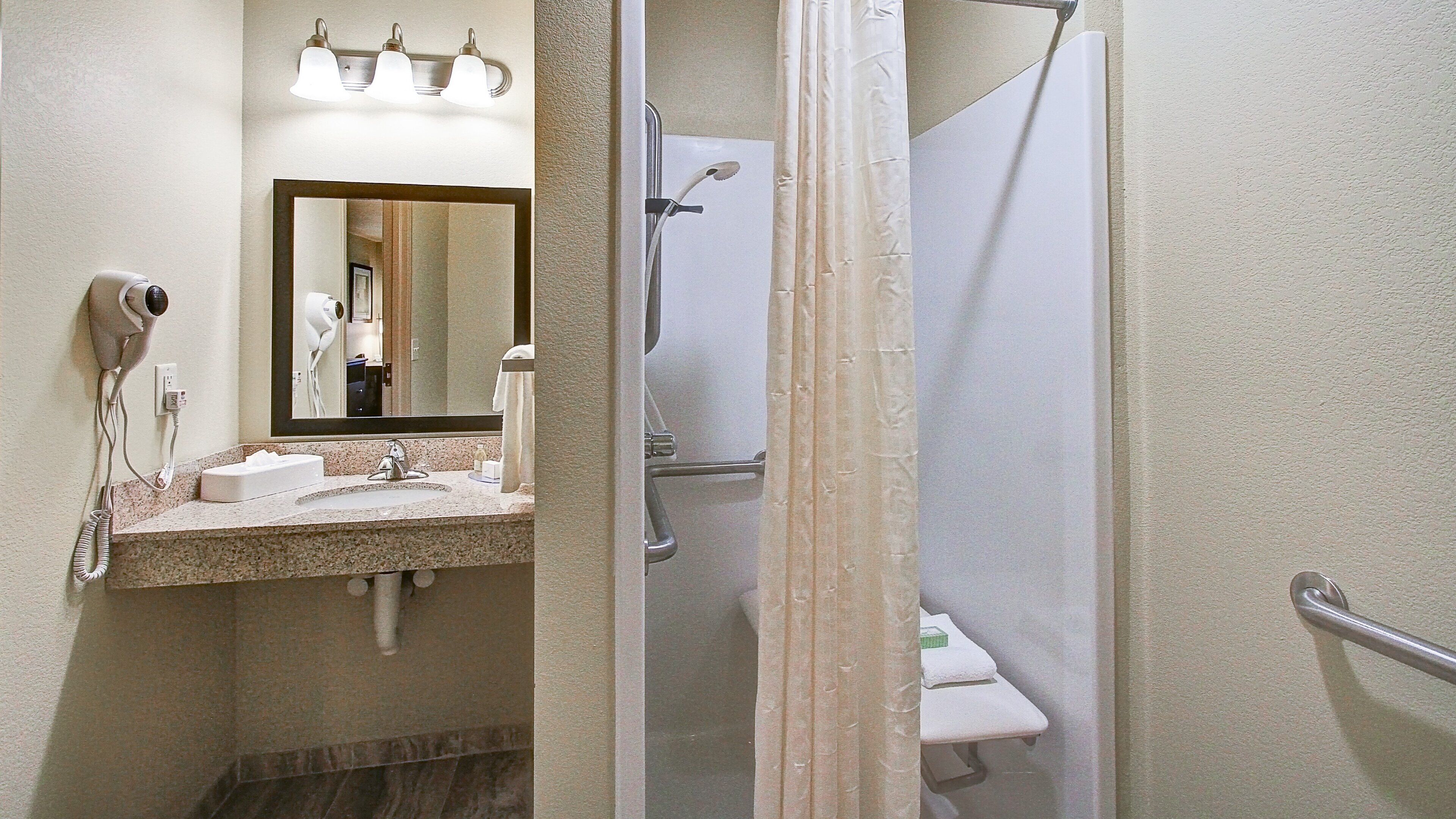 Un baño con lavamanos, espejo, secador de pelo y ducha.