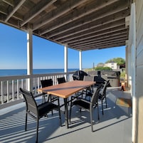 Un patio al aire libre con mesa y sillas de madera, una parrilla y vista al océano.