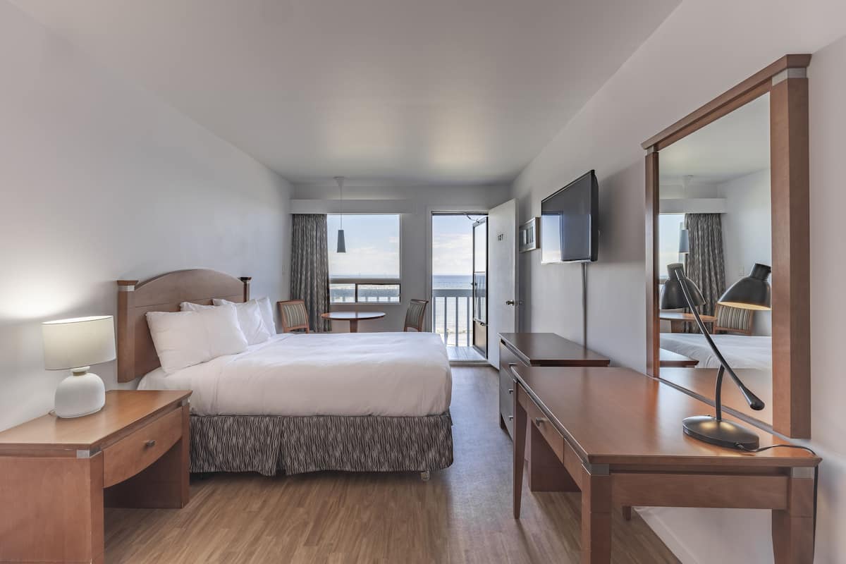 Ein Hotelzimmer mit Bett, Nachttisch, Schreibtisch, Stuhl, Fernseher und Meerblick.