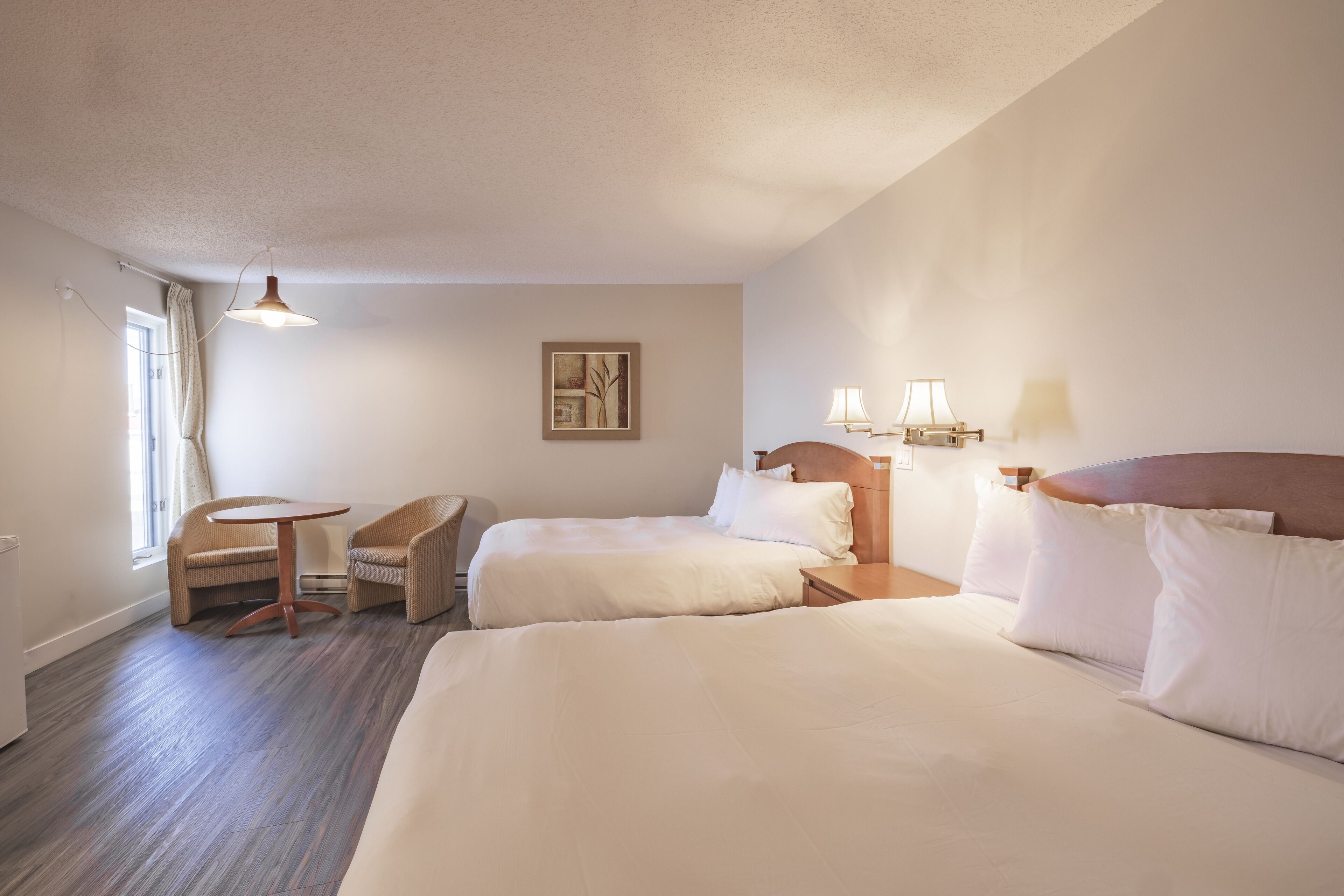 A hotel room with two beds, a small table, a chair, and a window with curtains.