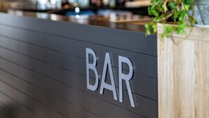 A bar area with a sign that reads "BAR" on the wall, shelves with bottles, and a hanging light fixture.