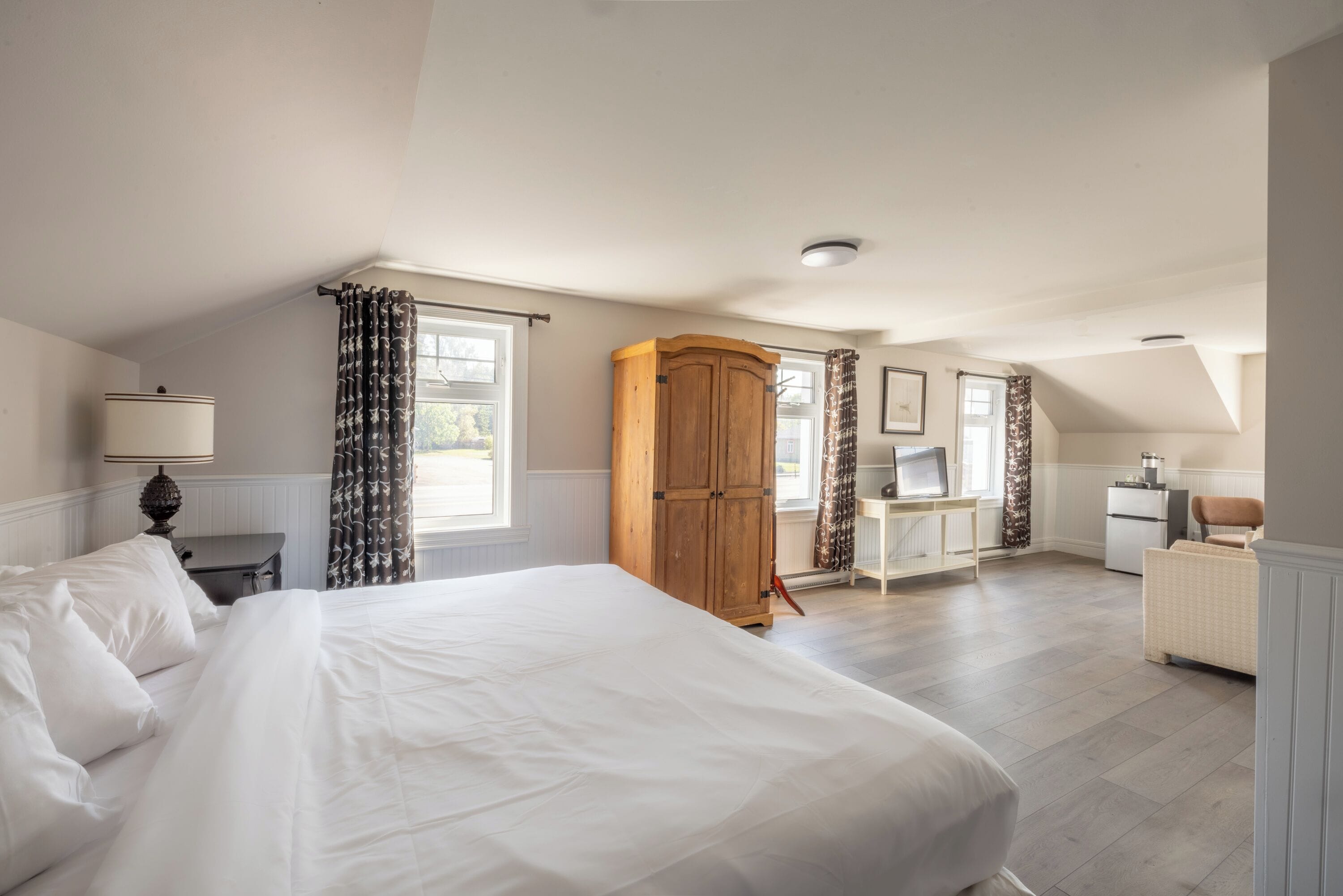 Un dormitorio con una cama grande, un armario de madera, un escritorio con silla y una pequeña kitchenette.