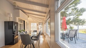 Una cocina moderna con un refrigerador negro, un comedor con mesa y sillas de vidrio, y vista a una terraza con mobiliario exterior.
