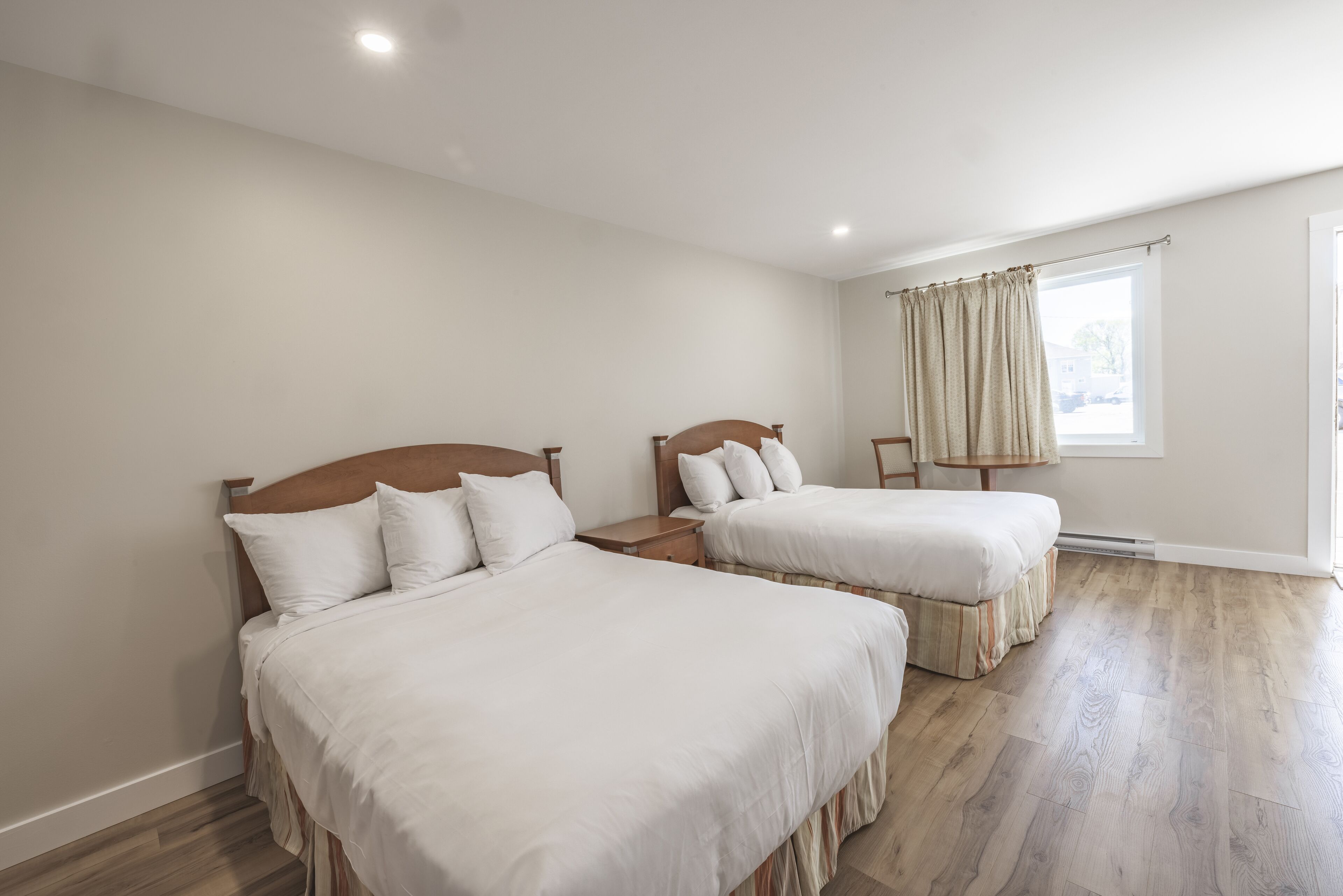 Habitación de hotel con dos camas individuales, un cabecero de madera, una ventana con cortinas y piso de madera.