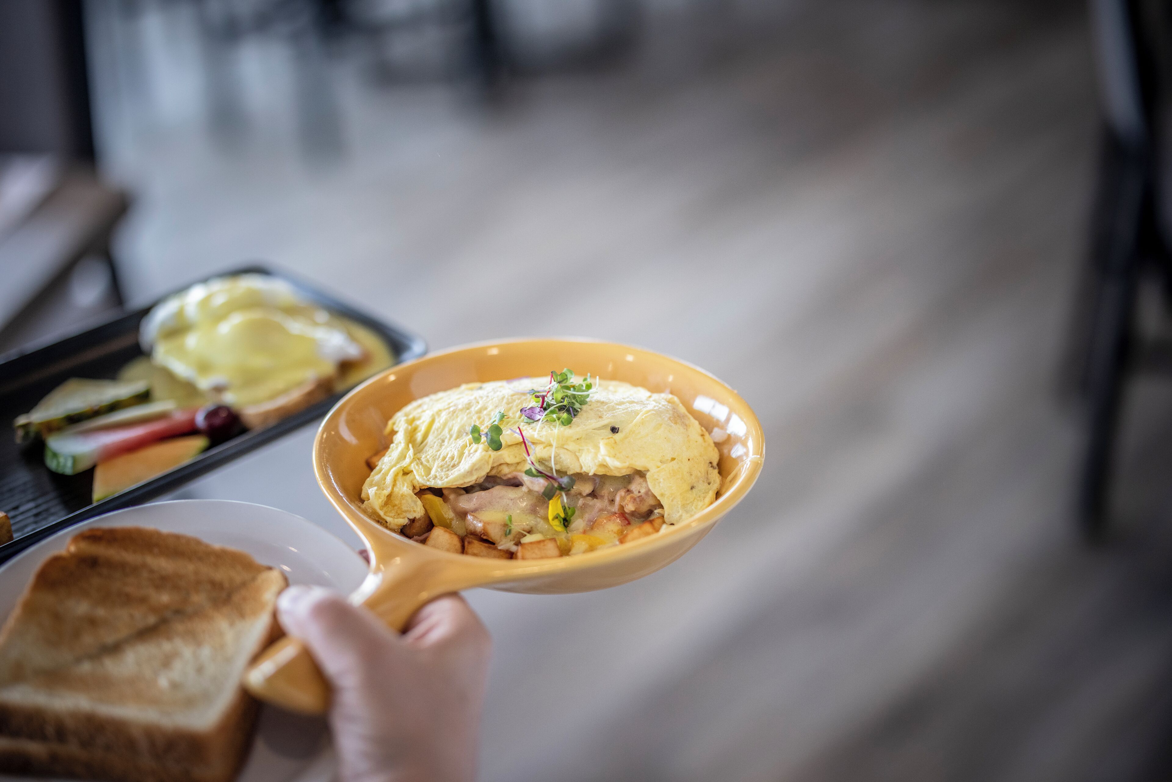 A hand holding a bowl of food with toast and a tray in the background.
