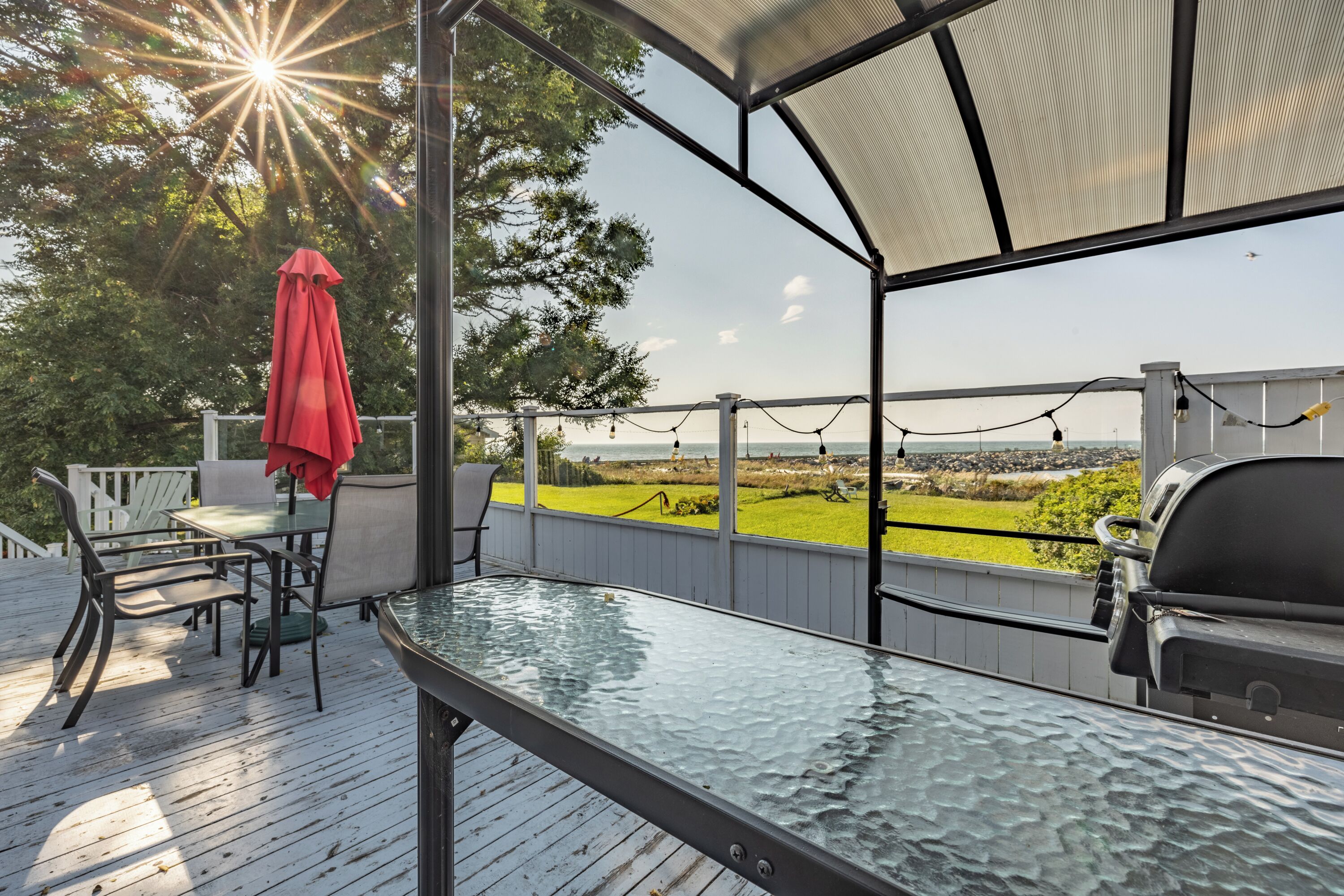A covered outdoor deck with a glass table, chairs, and a grill.
