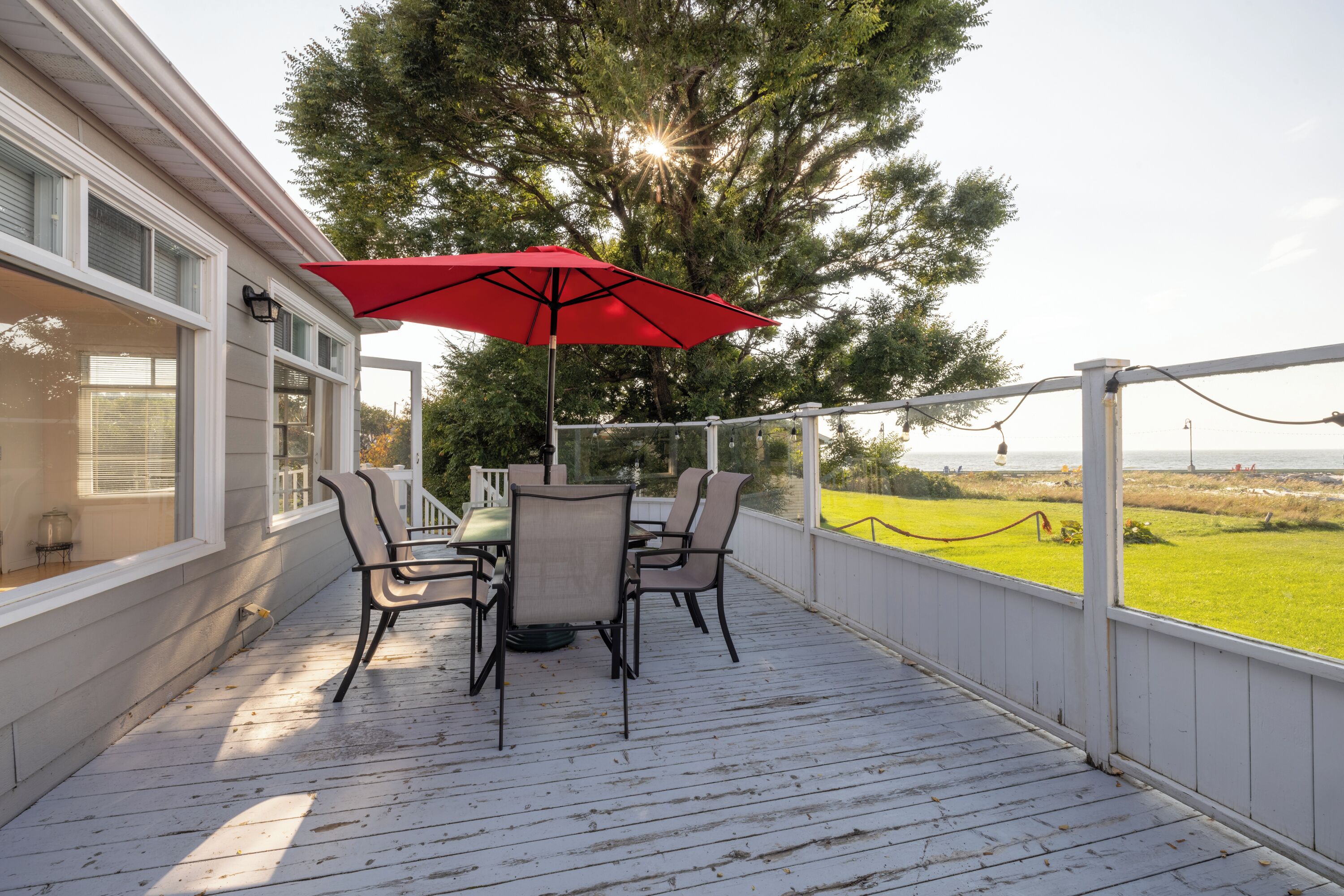 Une terrasse extérieure couverte, avec une table et des chaises, un parasol rouge et une vue sur le paysage.