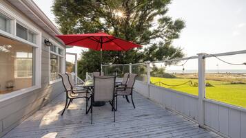 A covered outdoor patio with a table and chairs, a red umbrella, and a view of the landscape.