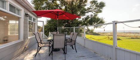 A covered outdoor patio with a table and chairs, a red umbrella, and a view of the landscape.