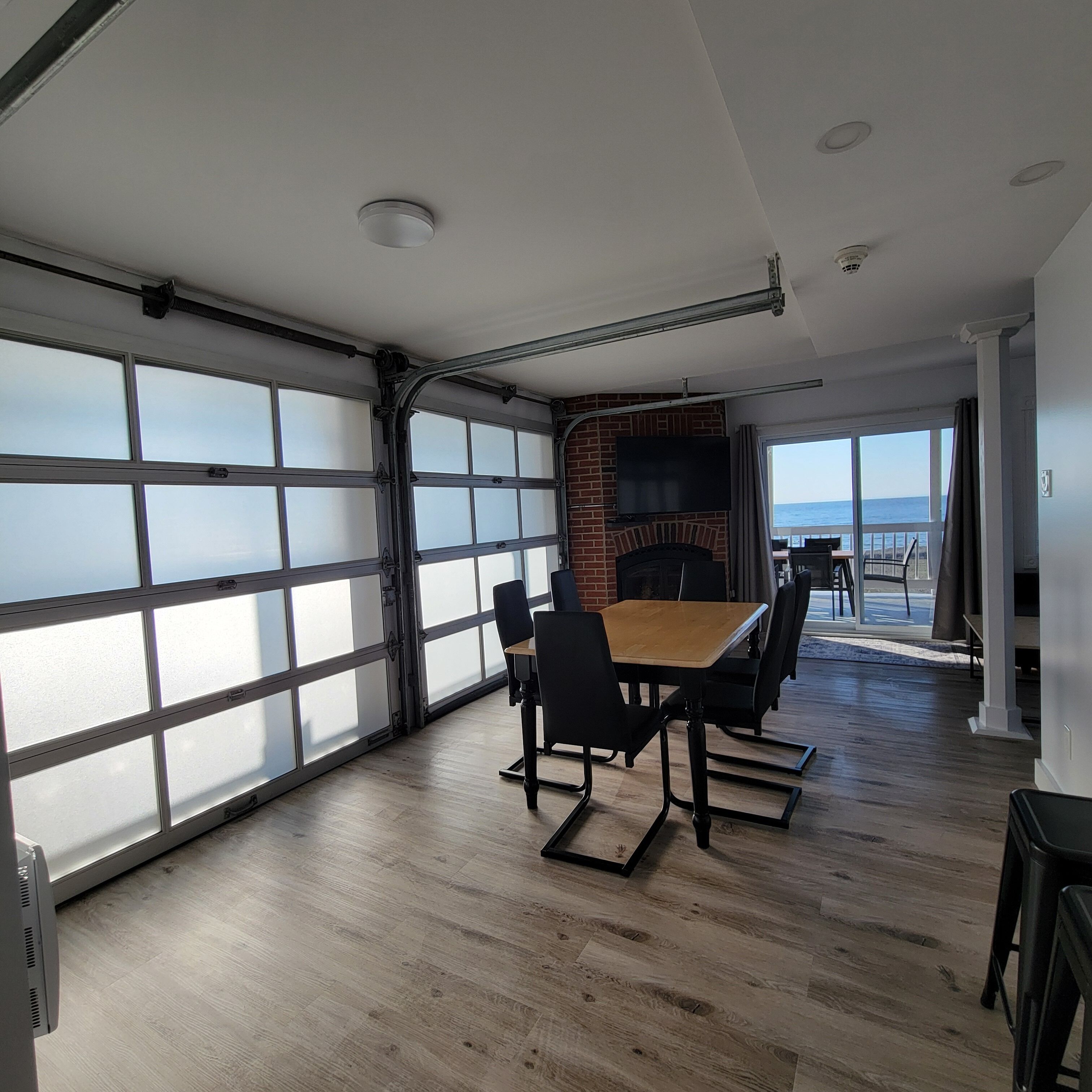 A spacious room with a large sliding glass door, a fireplace, a dining table with chairs, and a view of the ocean.
