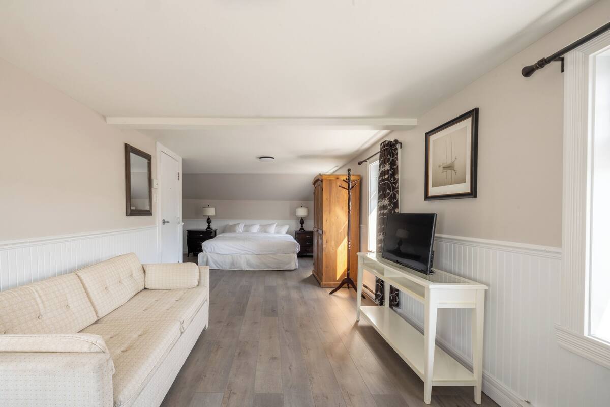 Ein Hotelzimmer mit Bett, Fernseher auf einem Schrank, einer Couch und einem Fenster mit Vorhängen.