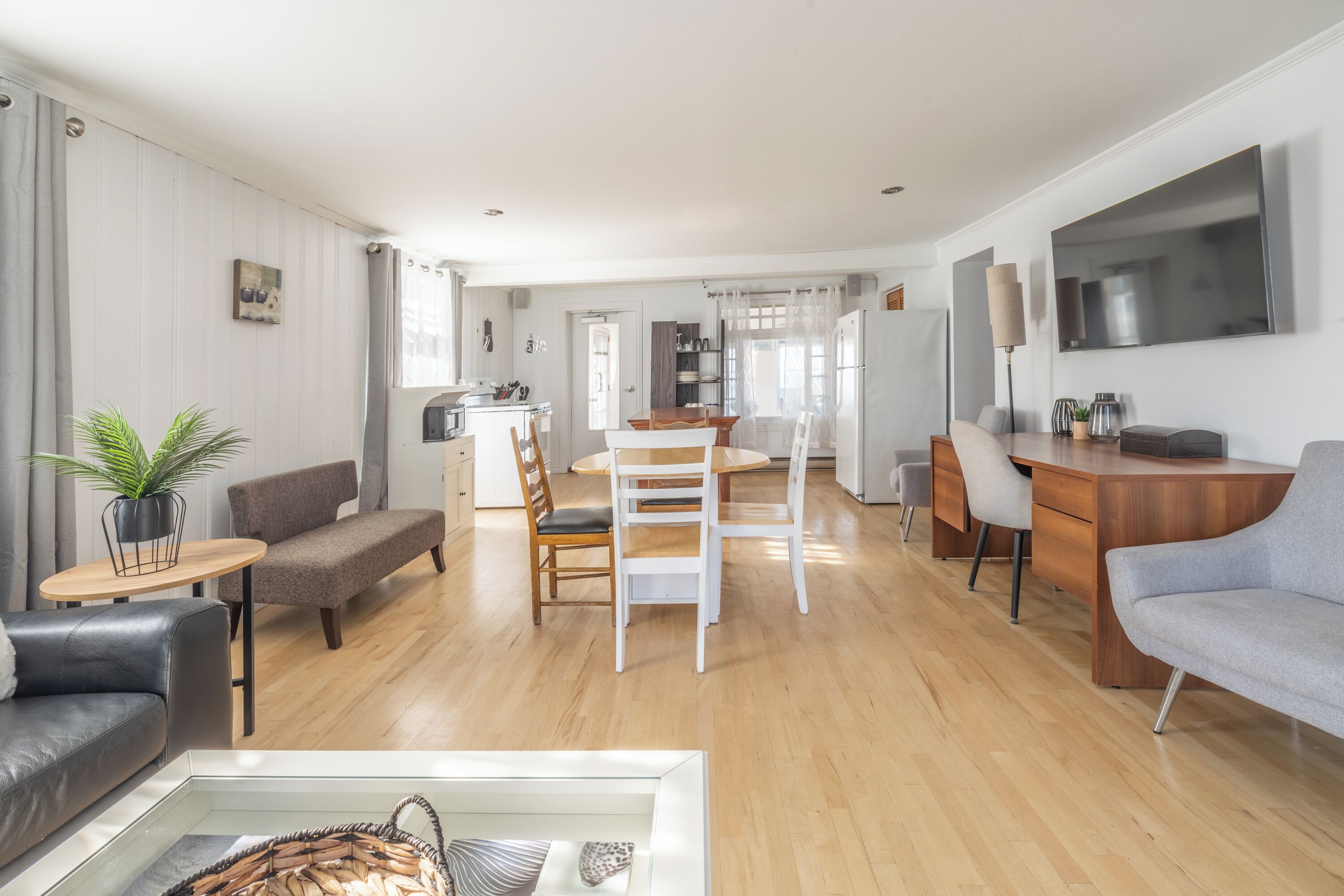 A spacious living area with a dining table, sofas, and a TV mounted on the wall.