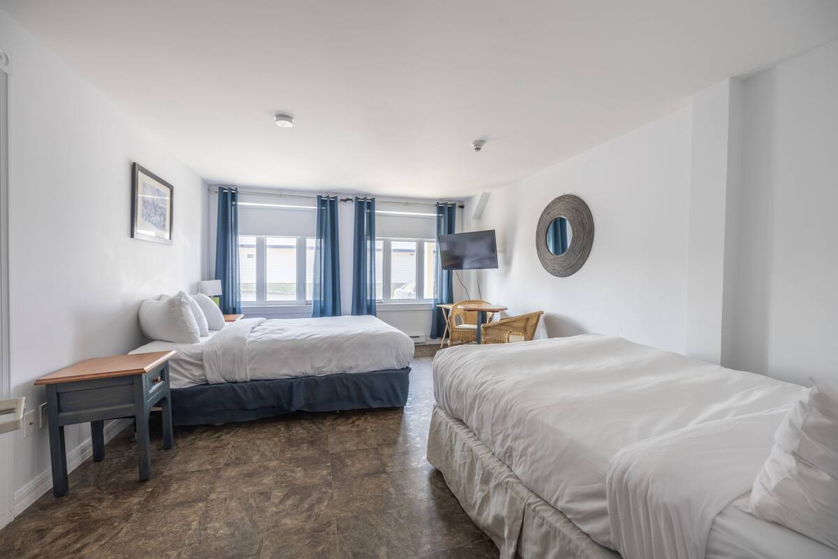 Ein Hotelzimmer mit zwei Betten, einem Schreibtisch, einem Sessel, einem Fernseher und einem Fenster mit Vorhängen.