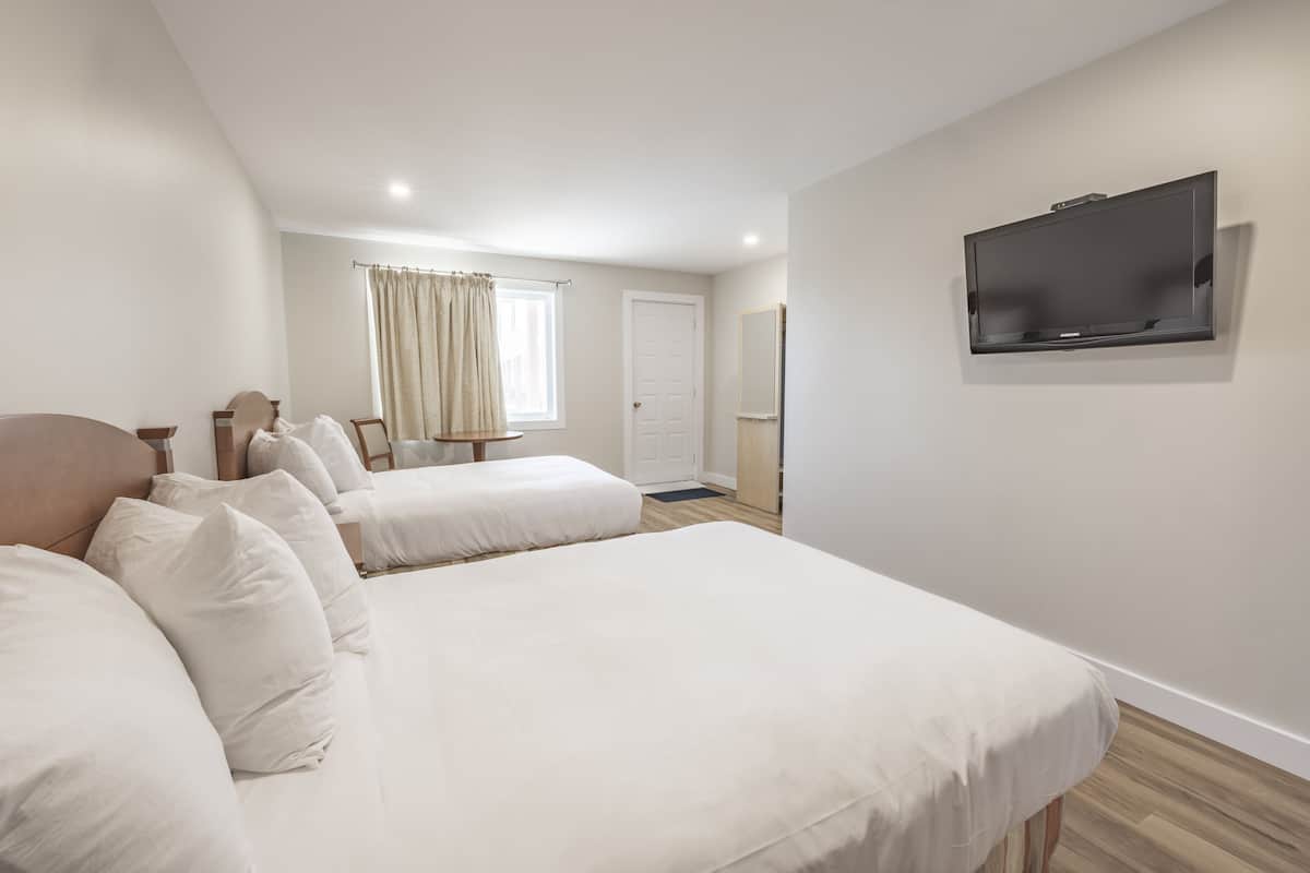 Ein Hotelzimmer mit zwei Betten, einem Fernseher, einem Fenster mit Vorhängen und einer Tür.
