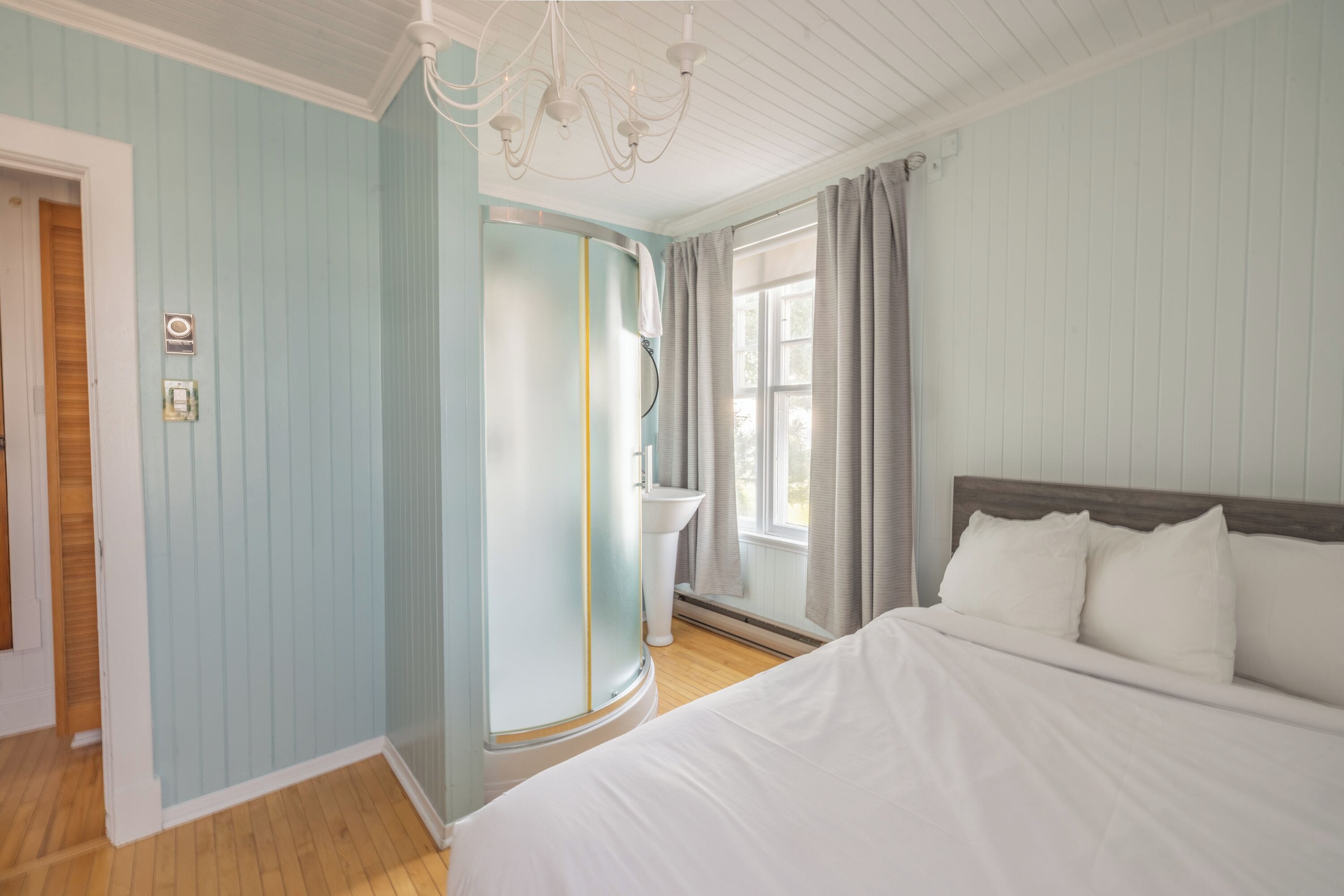 A bedroom with a bed, a nightstand, a dresser, a window with curtains, and a chandelier.
