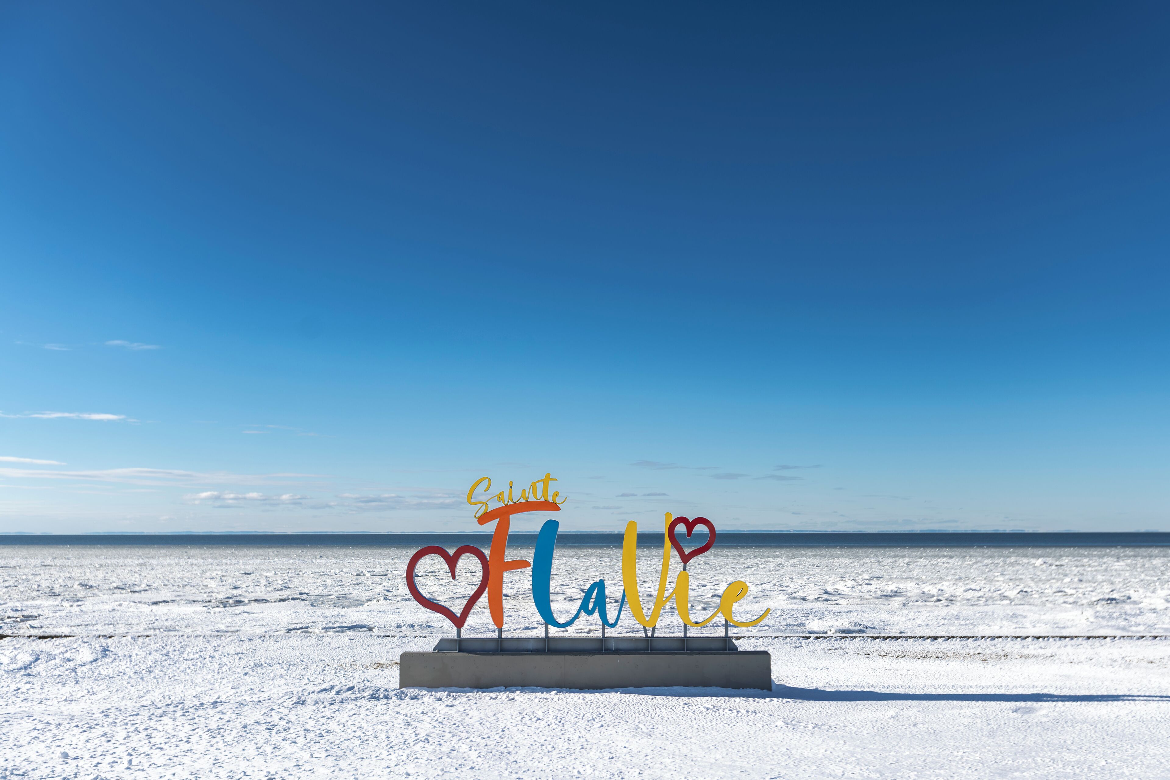 Une plage enneigée avec un panneau sur lequel on peut lire « Saïte Flavie », les lettres étant en forme de cœur.