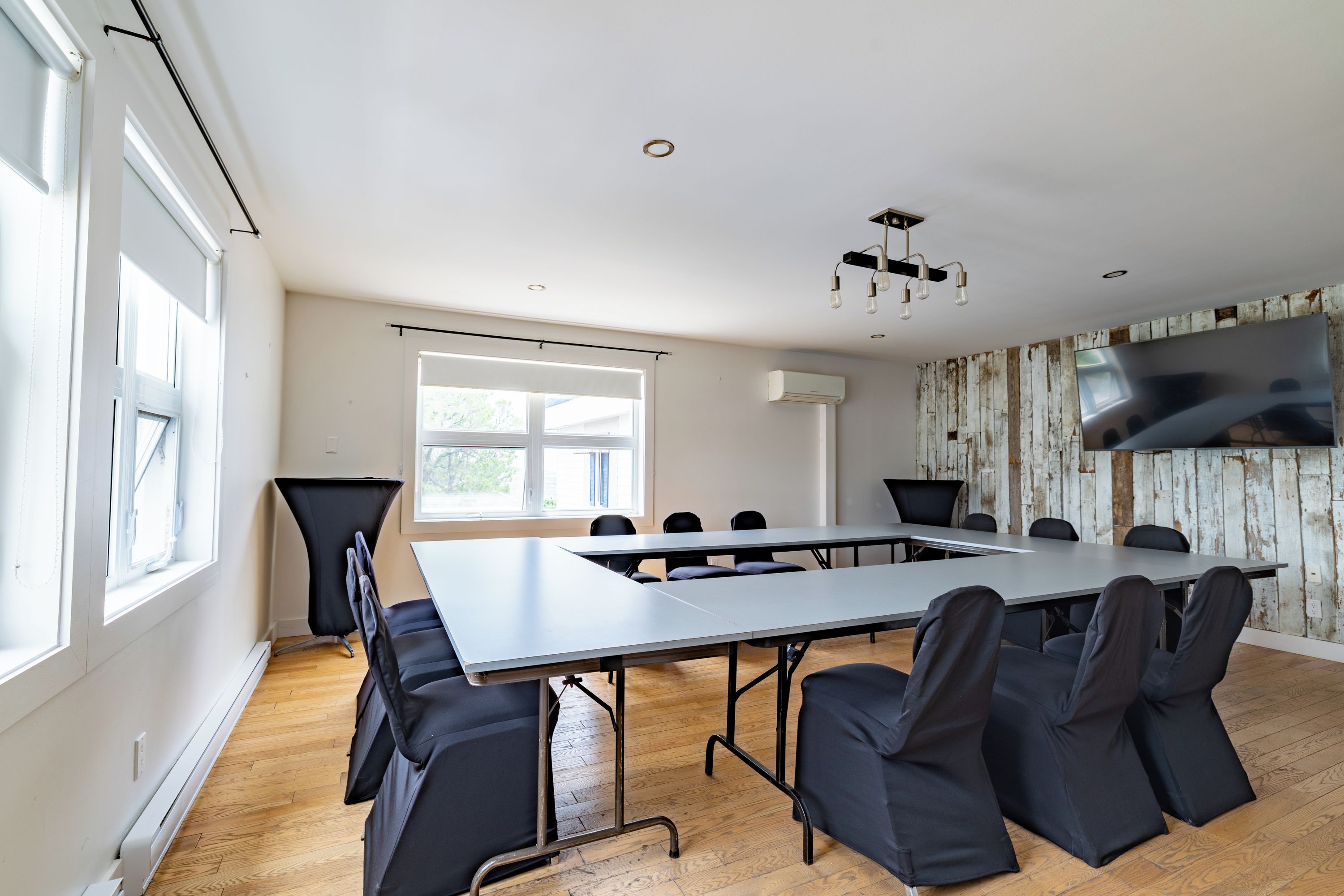 Een vergaderruimte met een lange tafel, zwarte stoelen, een plafondlamp en een groot raam.