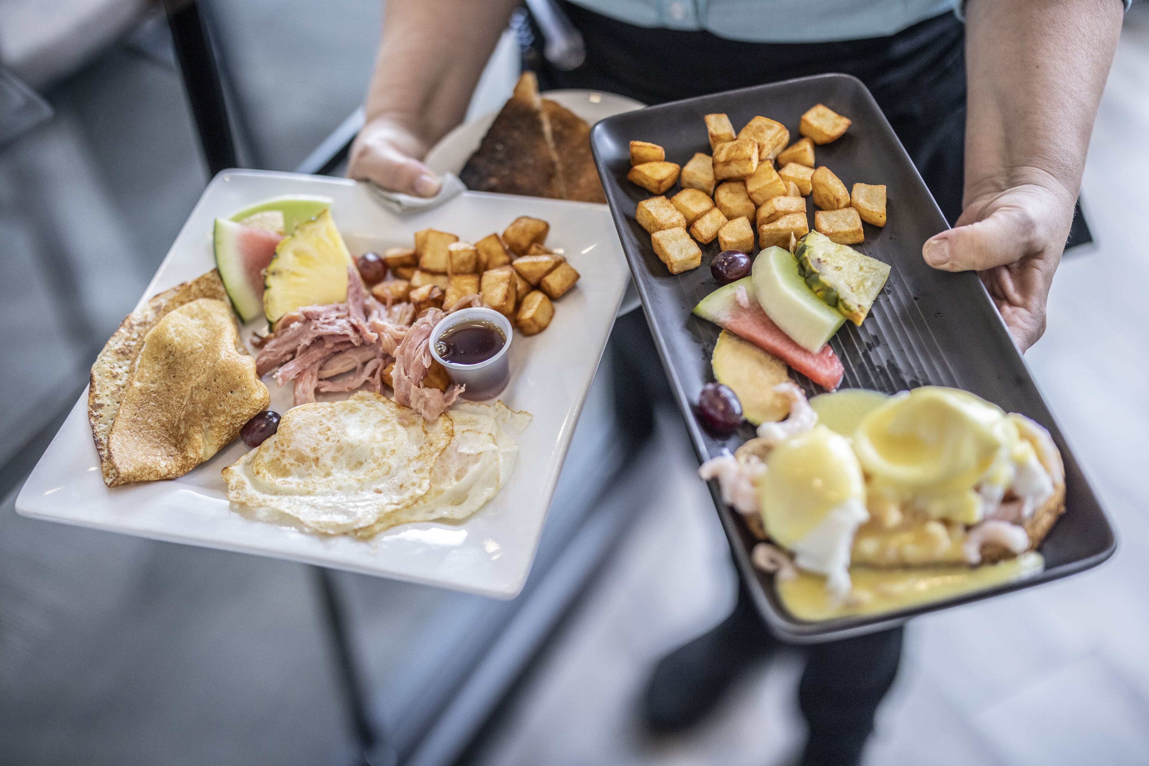 Un plateau contenant divers éléments pour le petit-déjeuner, notamment des toasts, des œufs, du jambon et des fruits.