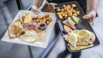 Un plateau contenant divers éléments pour le petit-déjeuner, notamment des toasts, des œufs, du jambon et des fruits.