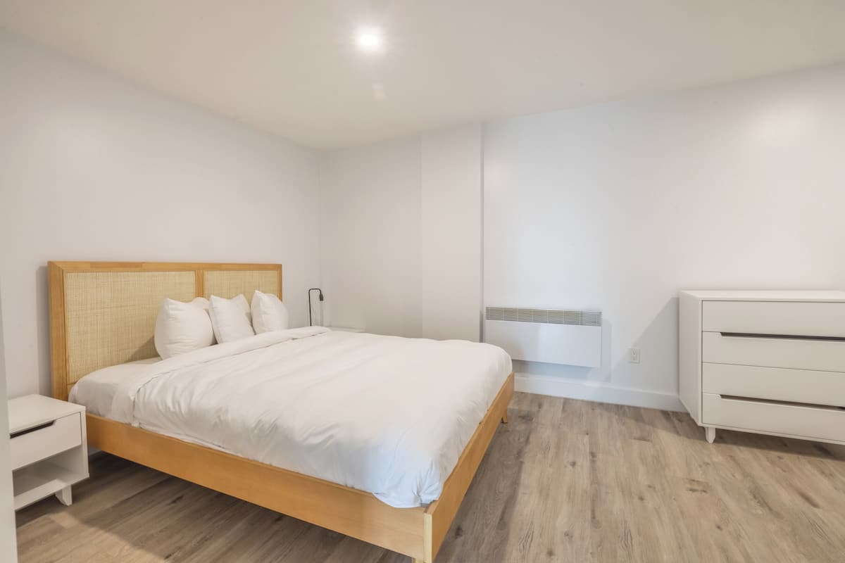 Ein Schlafzimmer mit einem hölzernen Bett, weißen Nachttischen, einer weißen Kommode und einem an der Wand montierten Heizkörper.