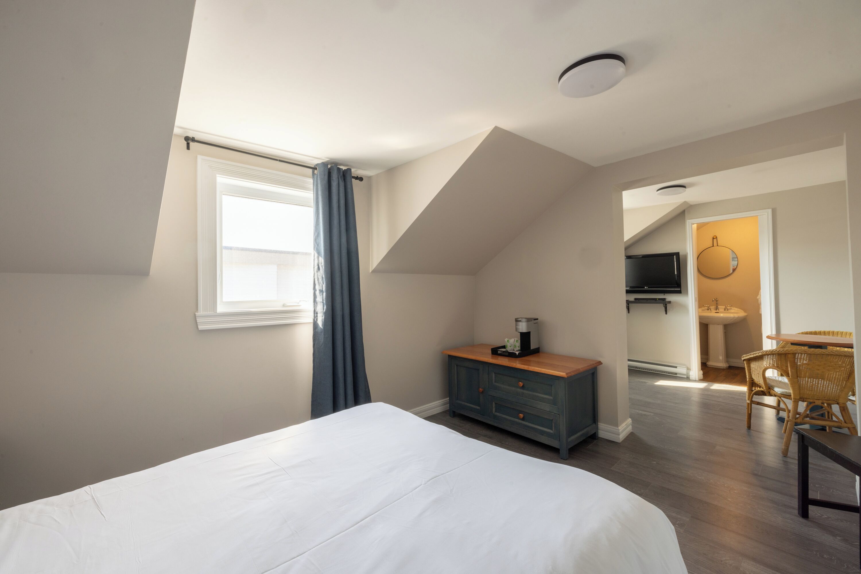 Une chambre à coucher avec un grand lit, une commode, un téléviseur et une salle de bain visible à travers une porte ouverte.