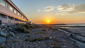 Un hotel costero con una larga edificación que domina la playa, un cielo despejado y el sol poniéndose en la distancia.