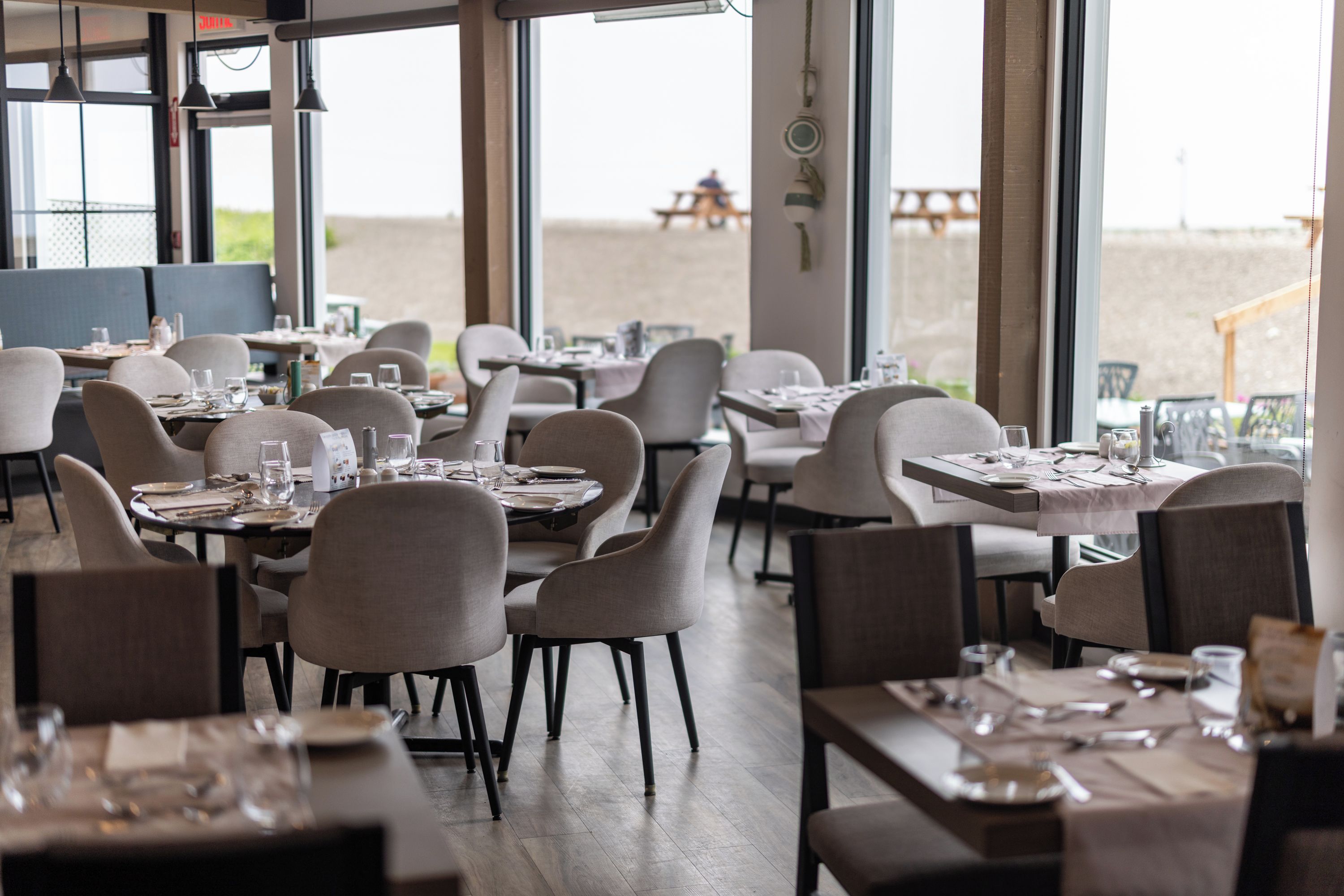 A restaurant with tables set for dining, chairs, and a view of the beach.