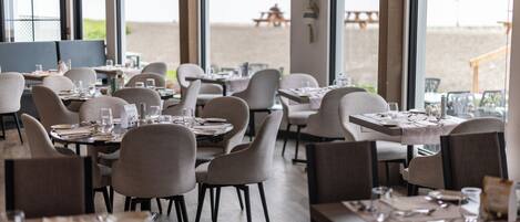 A restaurant with tables set for dining, chairs, and a view of the beach.