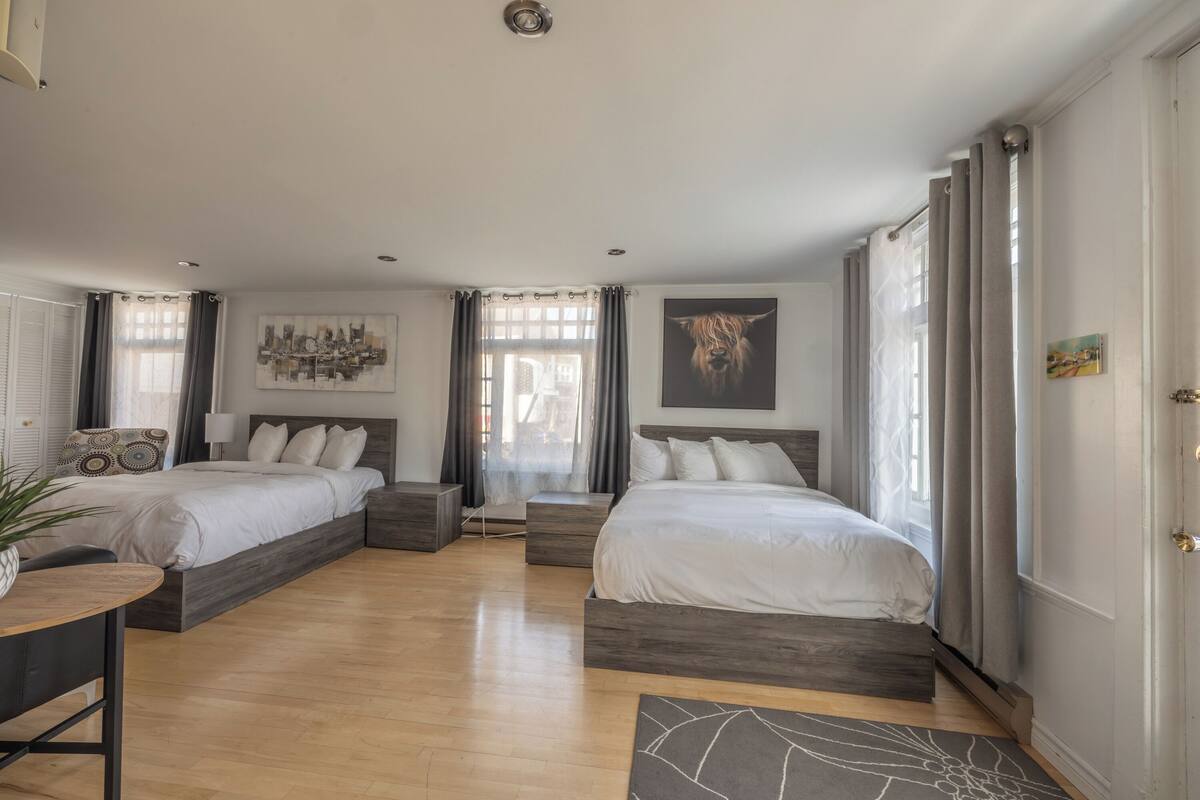 Ein geräumiges Schlafzimmer mit zwei Betten, einem Esstisch und einem großen Fenster mit Vorhängen.