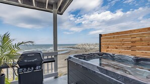 Un patio con una parrilla, un jacuzzi y vista a la playa.