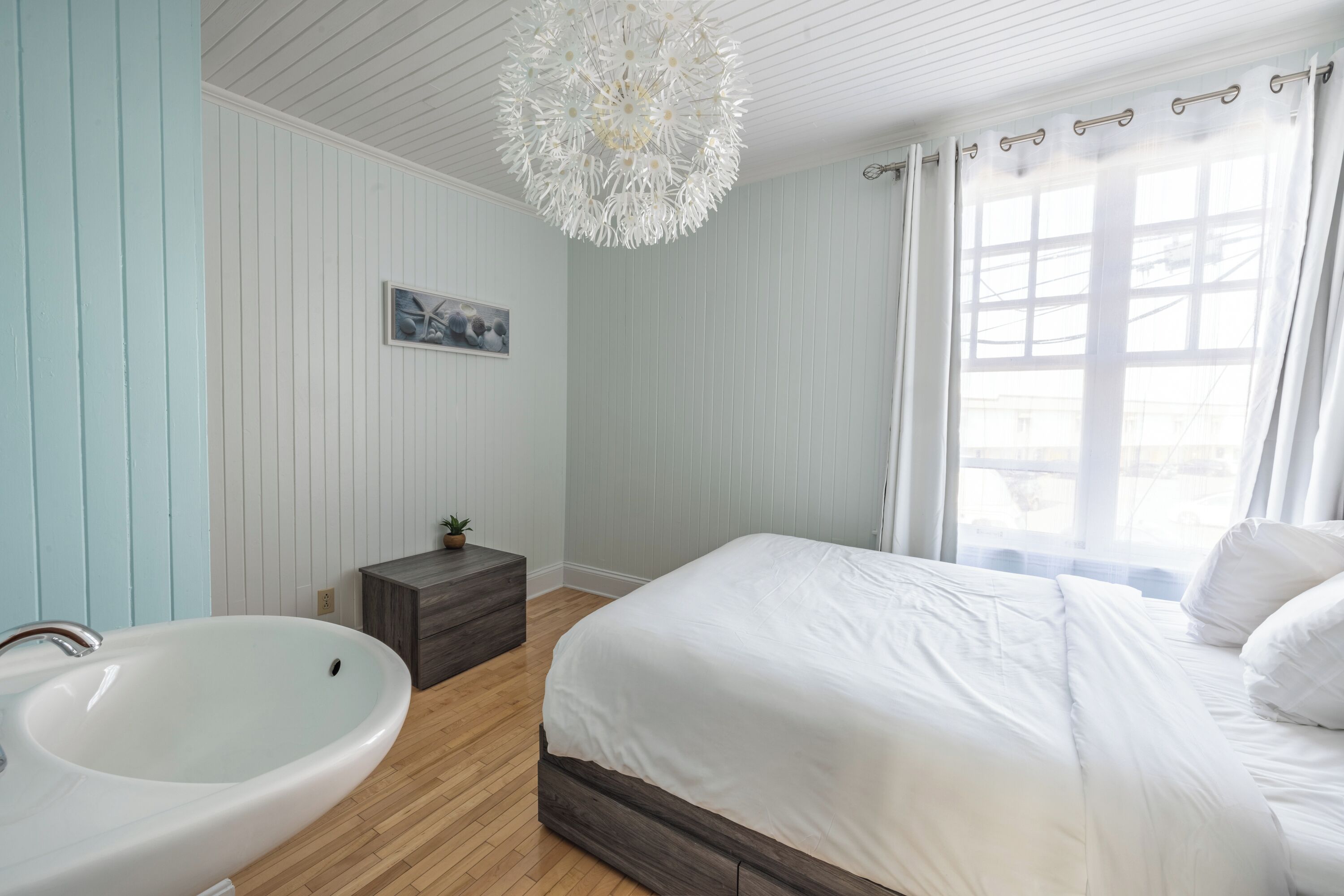 A bedroom with a large bed, a white sink, and a wooden floor.