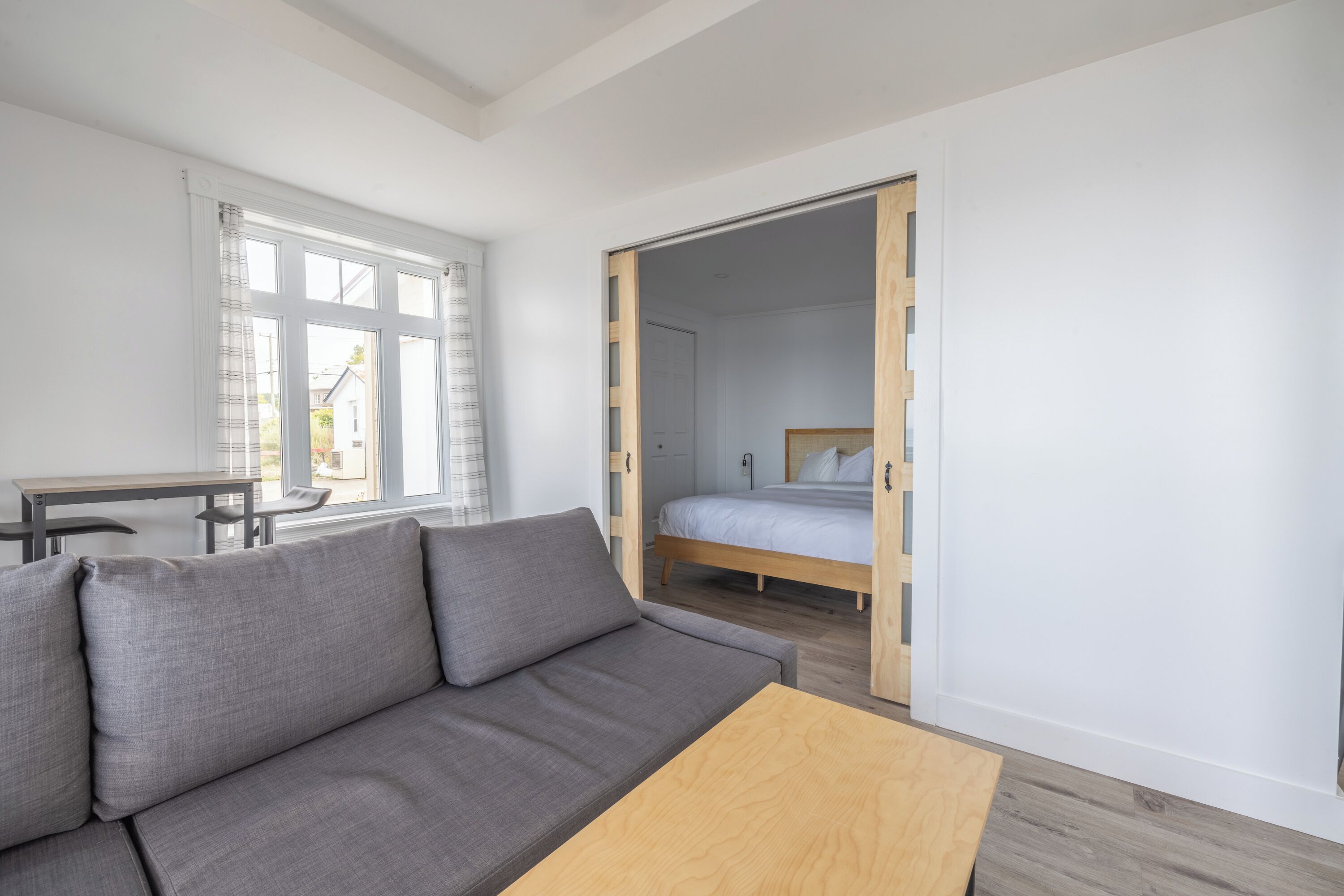 A modern room with a grey sofa, wooden coffee table, and a bed with a wooden headboard.