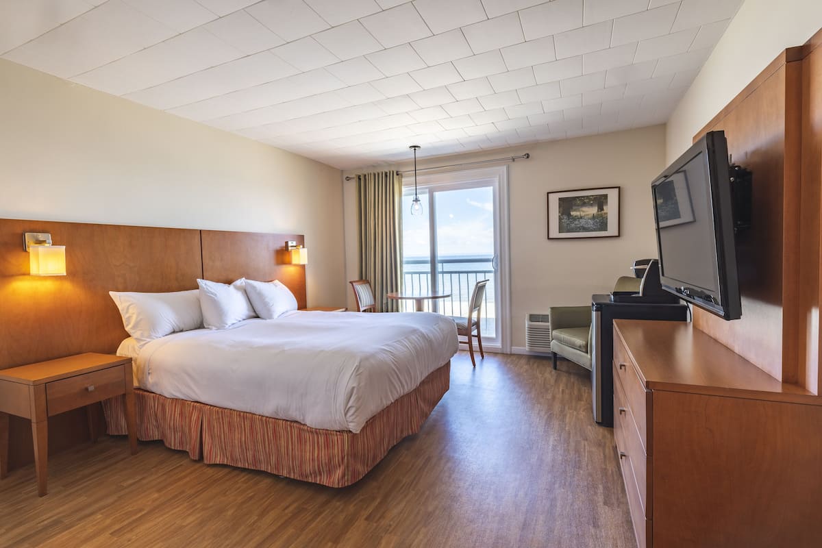 Ein Hotelzimmer mit einem großen Bett, Nachttischlampen, einem Fernseher, einem Schreibtisch und einem Sessel.